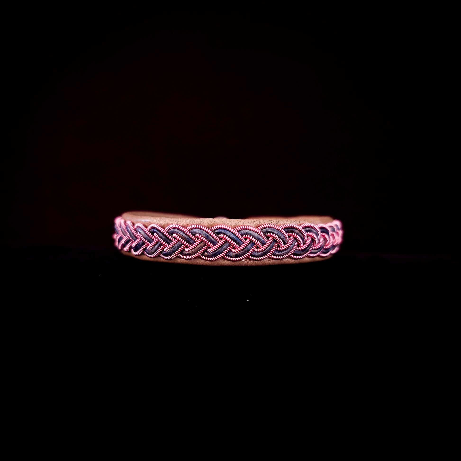 Bracelet with pink and black braided design on a black background