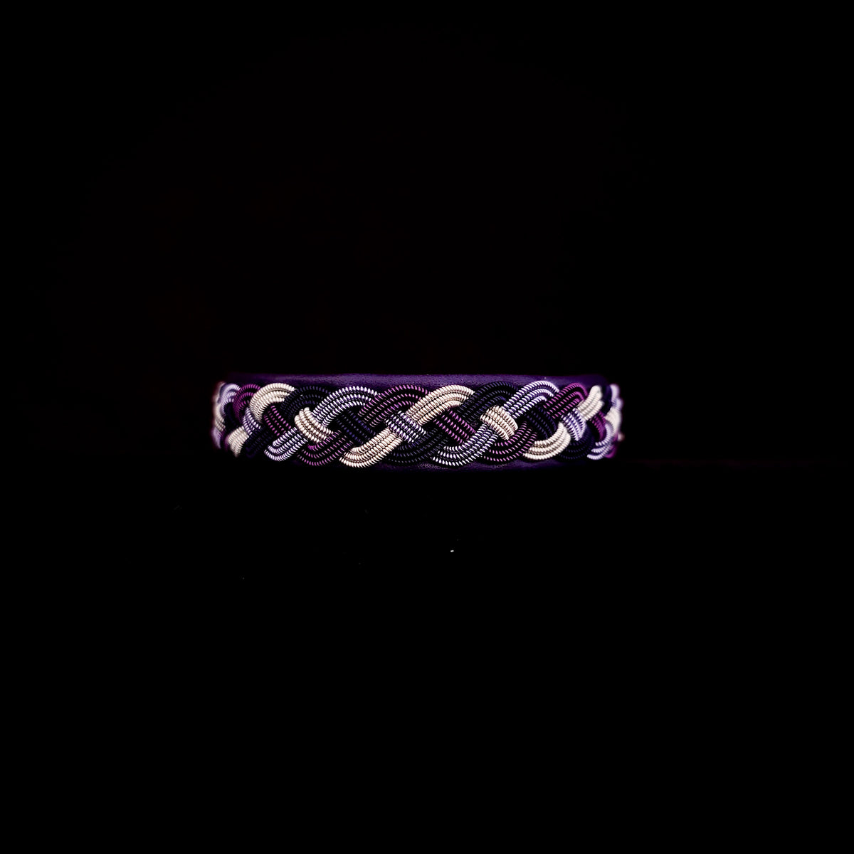 Braided bracelet with purple and silver tones on a black background