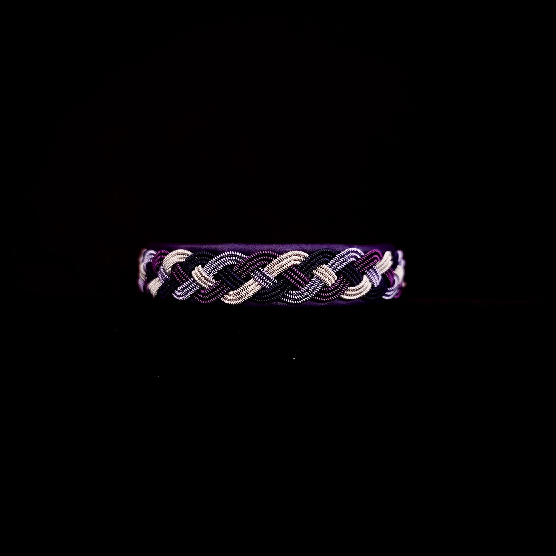 Braided bracelet with purple and silver tones on a black background